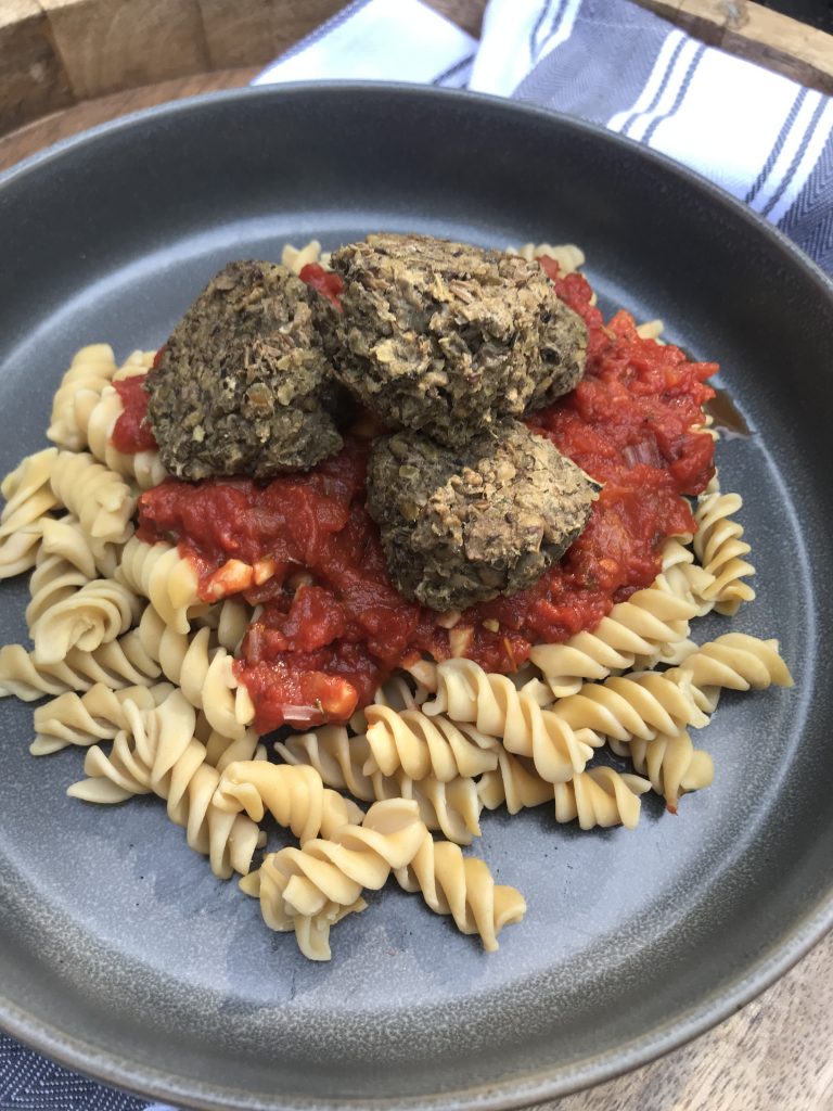 lentil meatballs on top of marinara sauce and rotini noodles