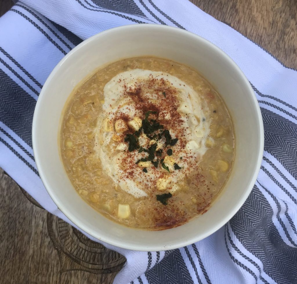 a bowl of corn chowder topped with cashew cream, paprika, and basil