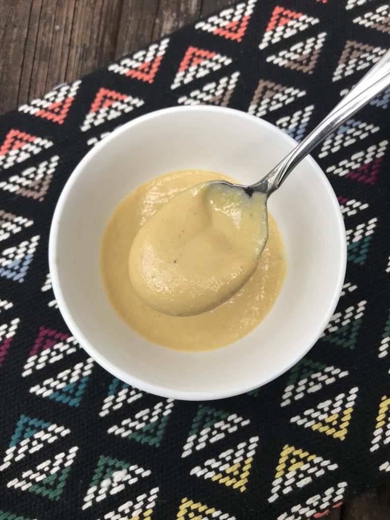 A bowl of yellow nutritional yeast dressing with a spoon taking a scoop