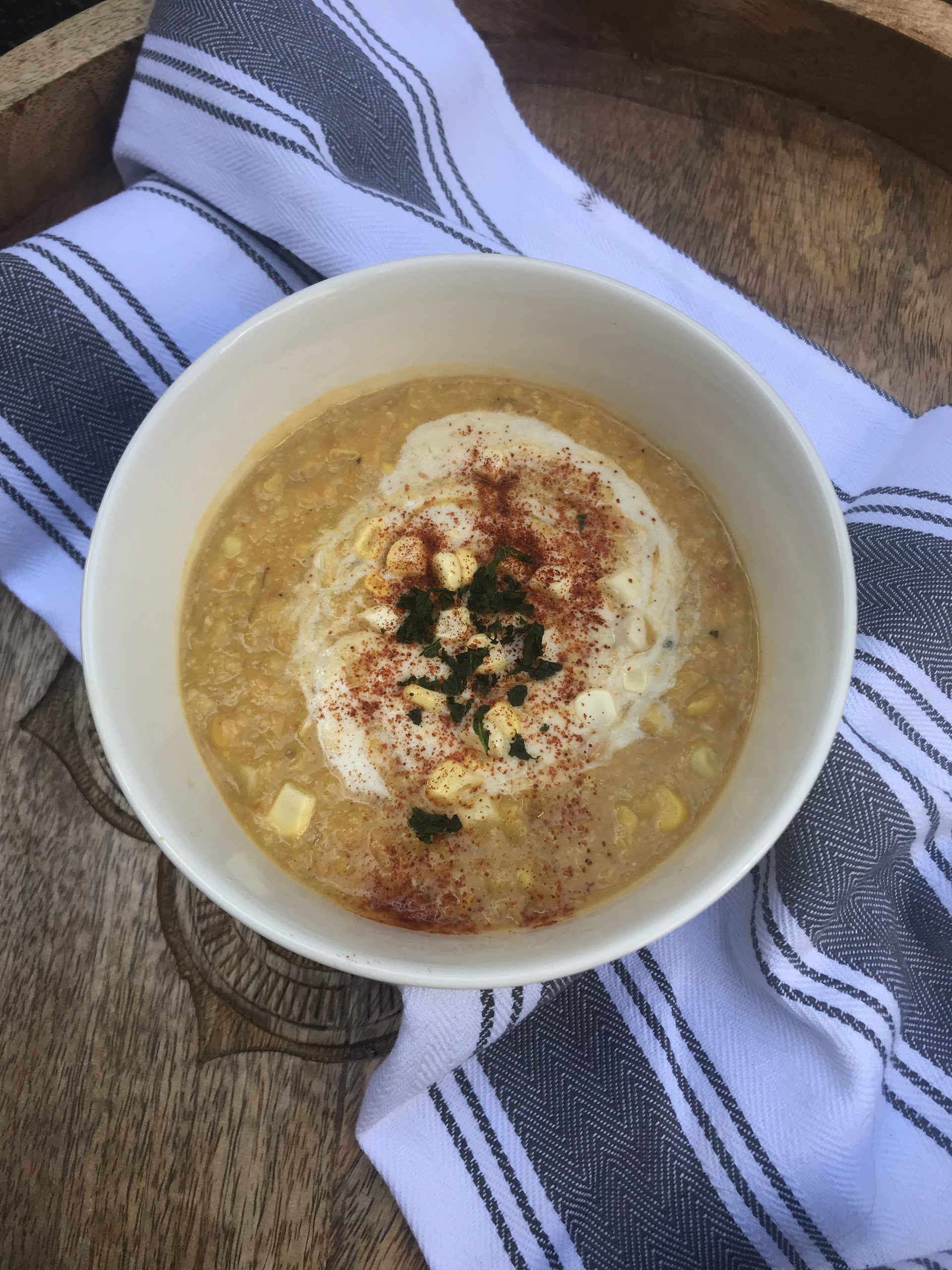 a bowl of corn chowder topped with cashew cream, paprika, and basil