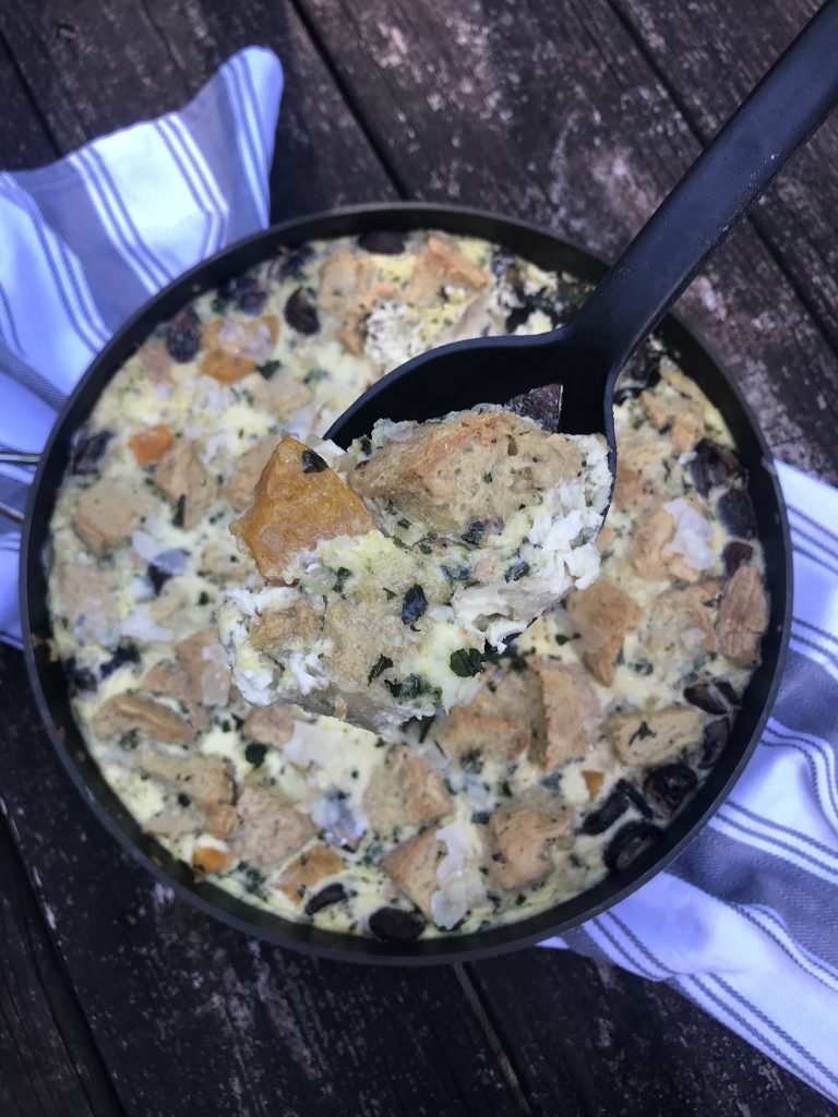 A spoon lifting out a scoop of bread pudding with butternut squash and mushrooms.