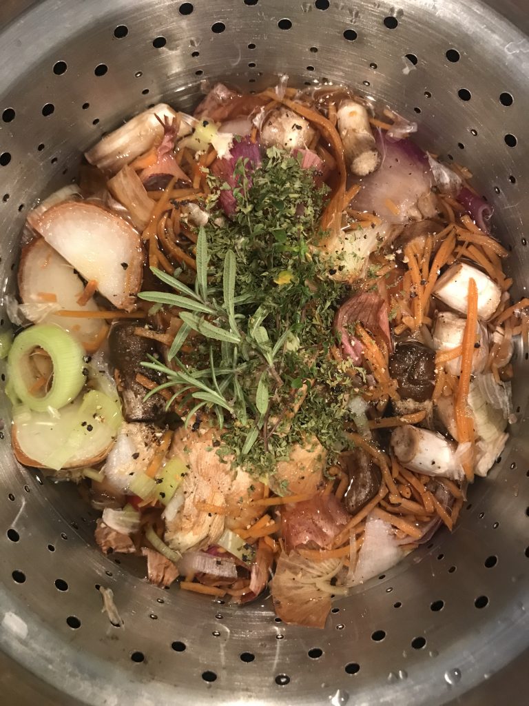 A stock pot with vegetables craps, water, and herbs on top