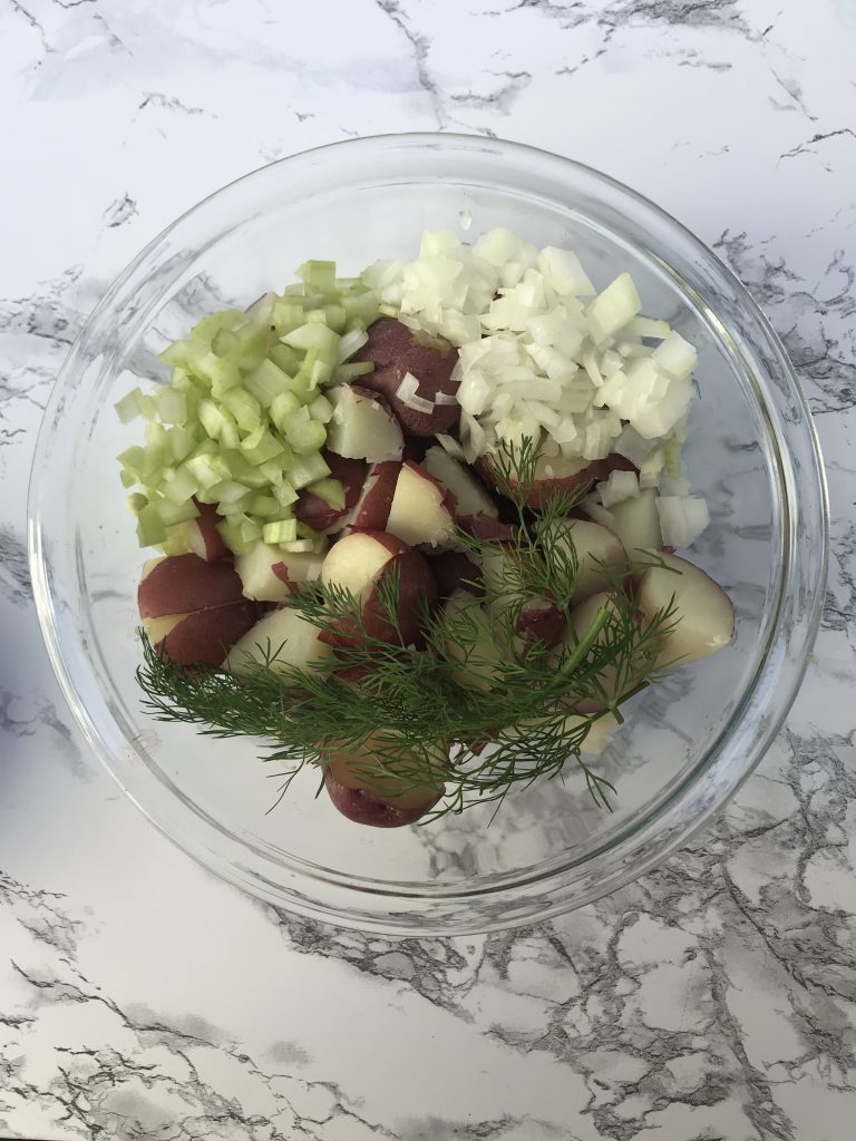 a bowl of potatoes, diced onion, diced celery, and dill