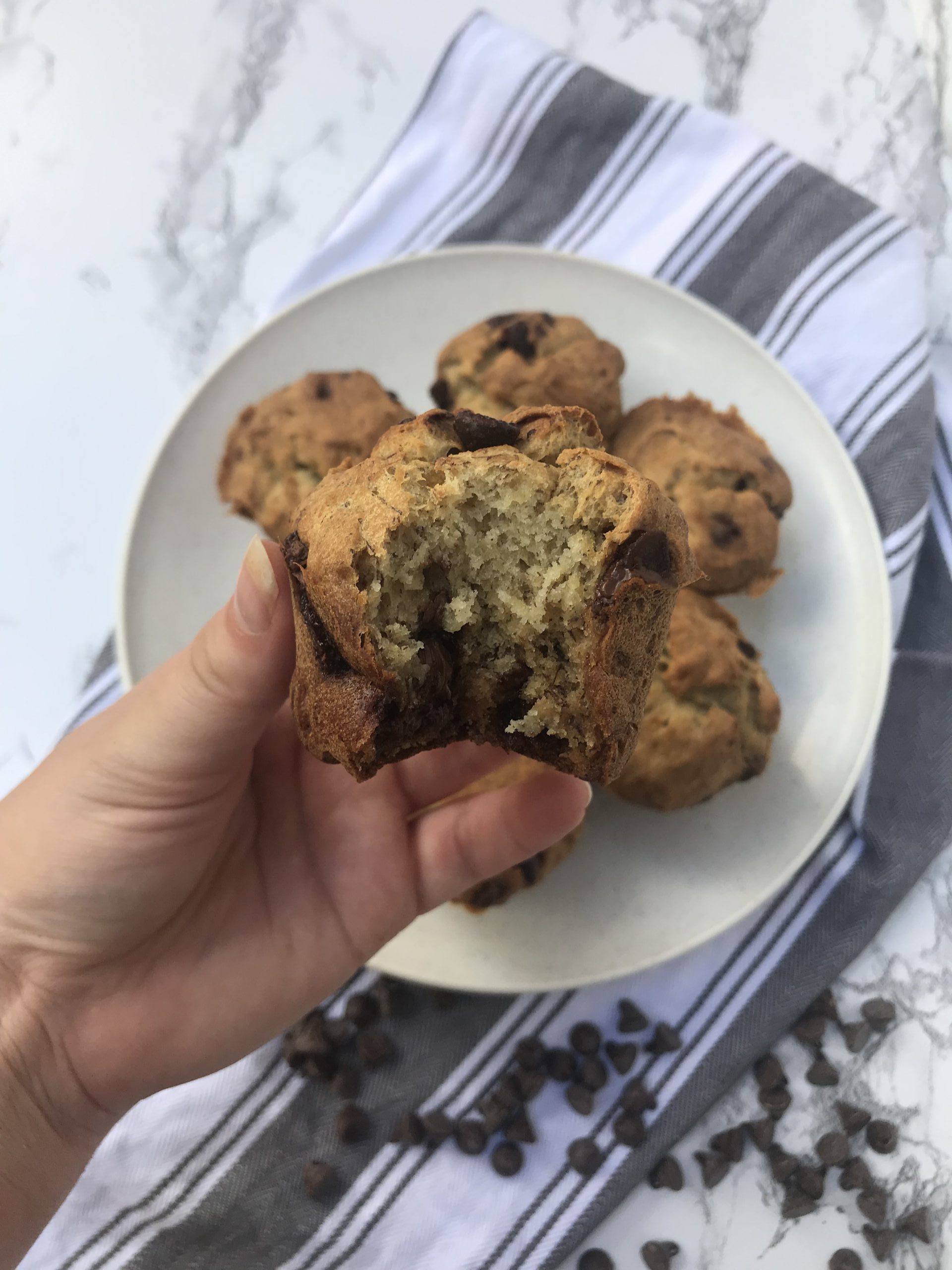 a hand holding up a banana bread muffin with a bite taken out