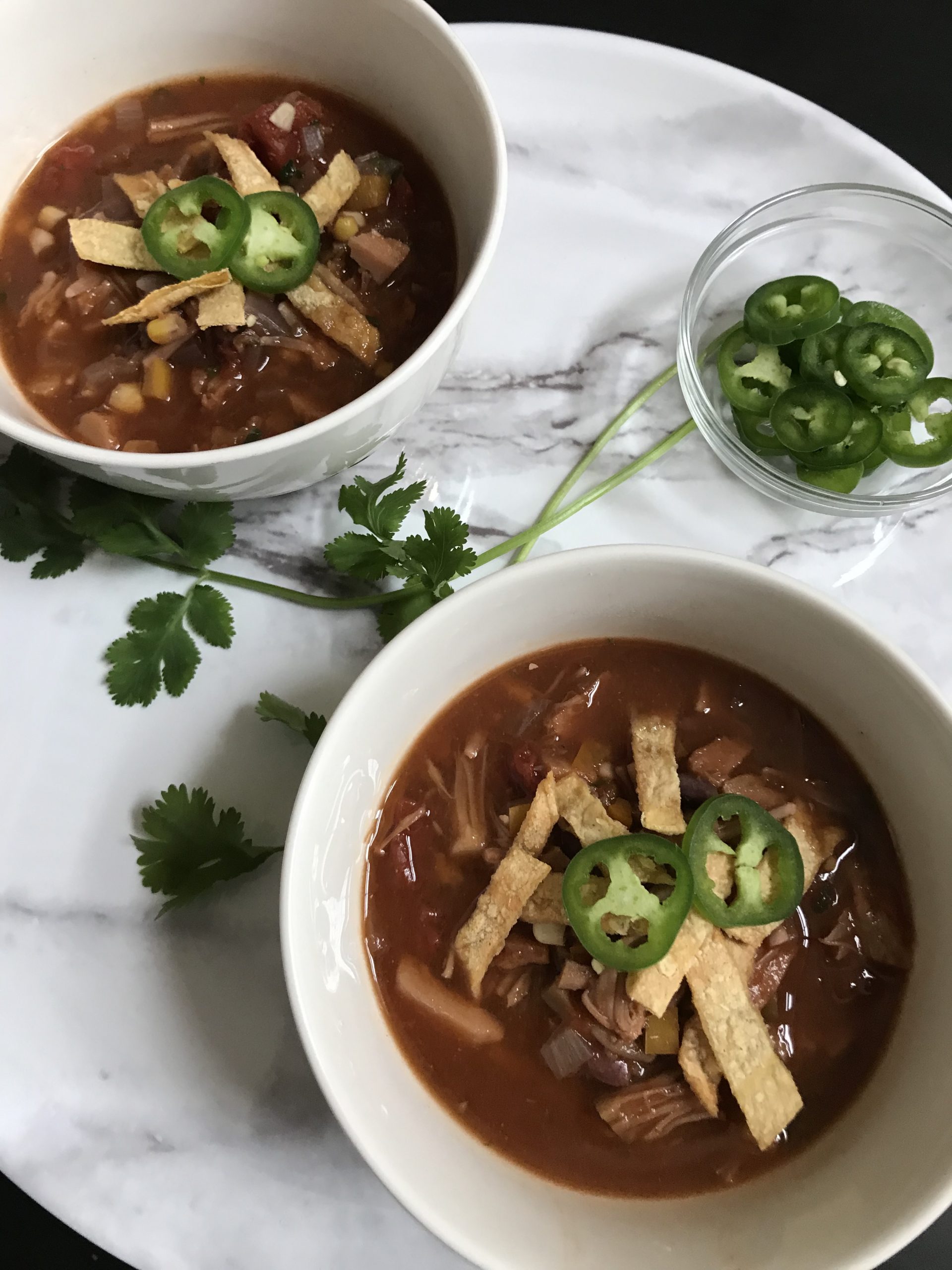 bowls of jackfruit tortilla soup topped with tortilla strips and jalapenos