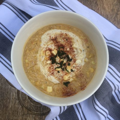 a bowl of corn chowder topped with cashew cream, paprika, and basil