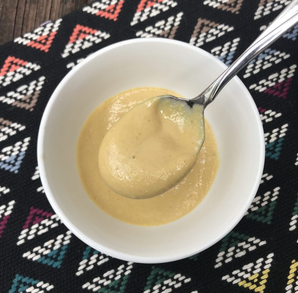 A bowl of yellow nutritional yeast dressing with a spoon lifting some sauce up