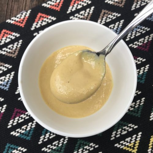 A bowl of yellow nutritional yeast dressing with a spoon lifting some sauce up