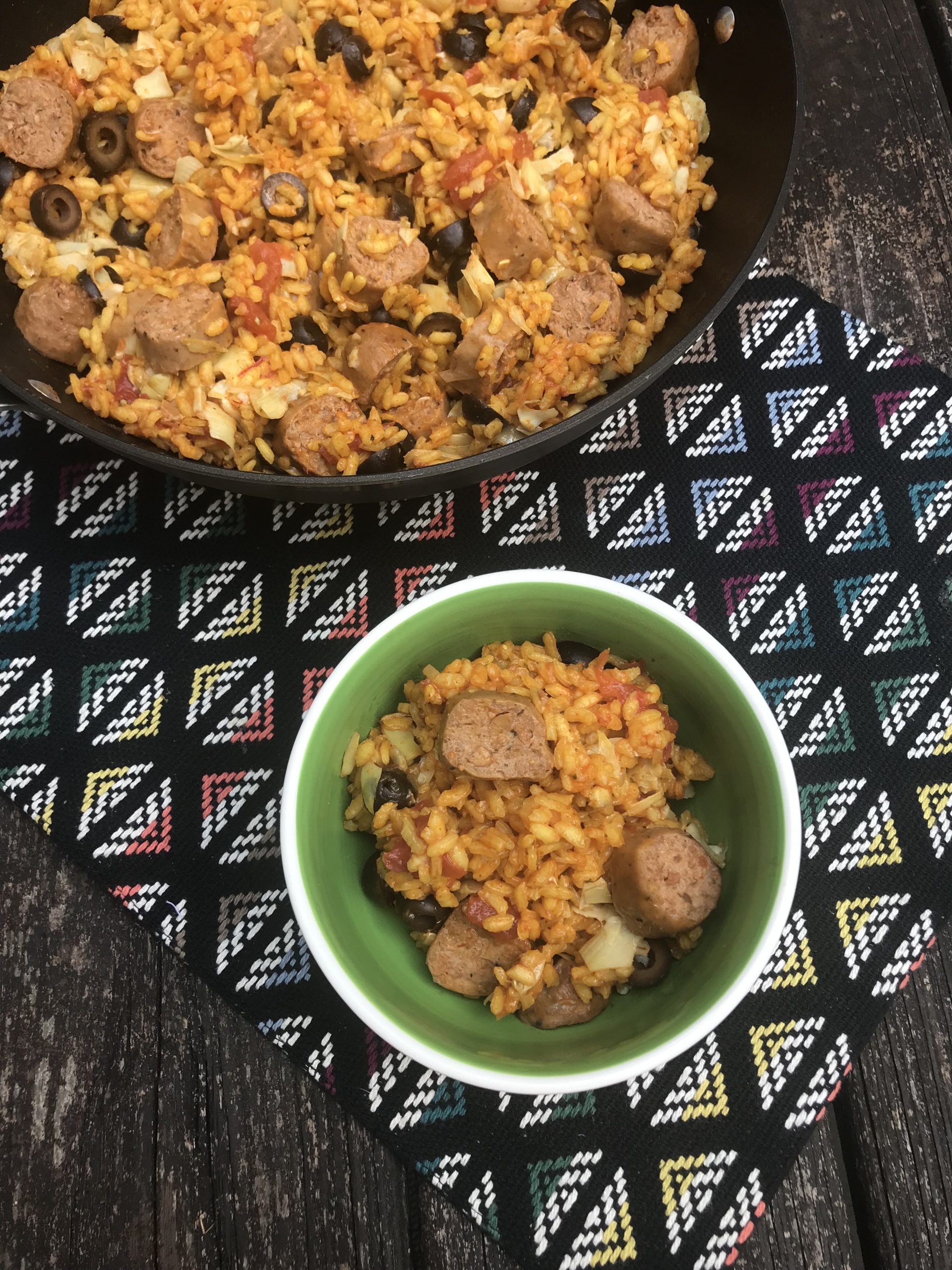 A bowl of paella with plant-based sausage slices on top.