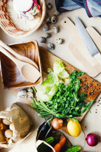 an overhead shot of a cutting board with veggies, knives, and serving utensils