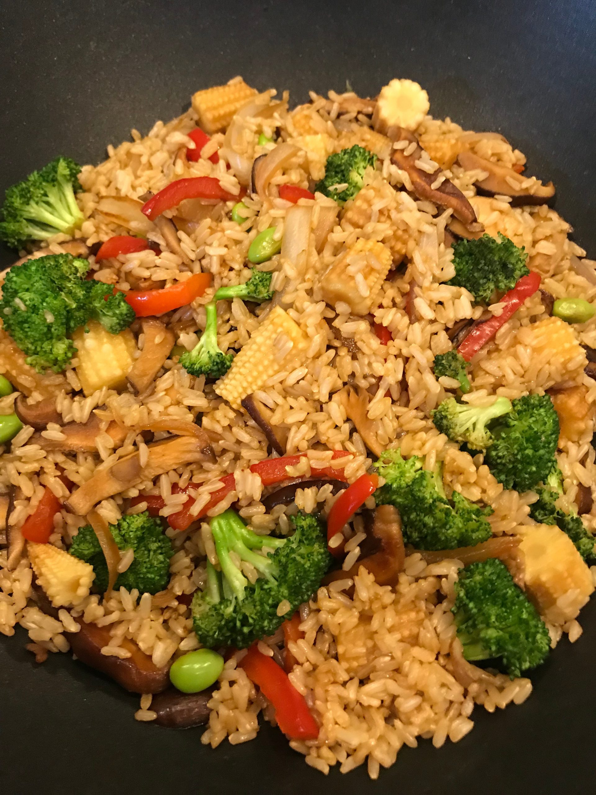 A wok of vegetable fried rice with broccoli, mushrooms, and baby corn