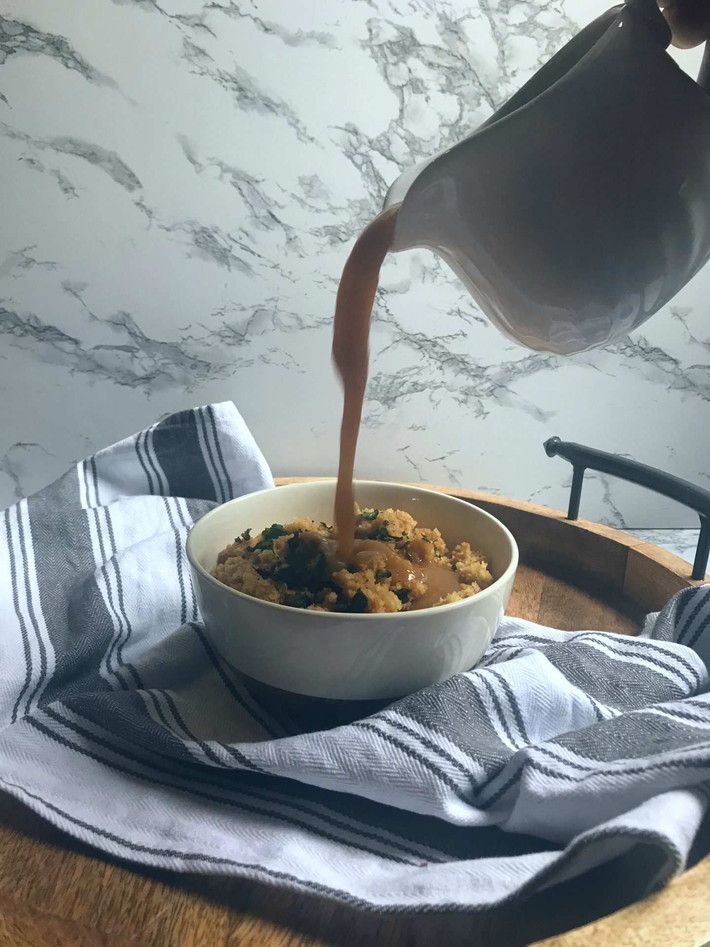 a gravy boat poring gravy into a bowl of stuffing