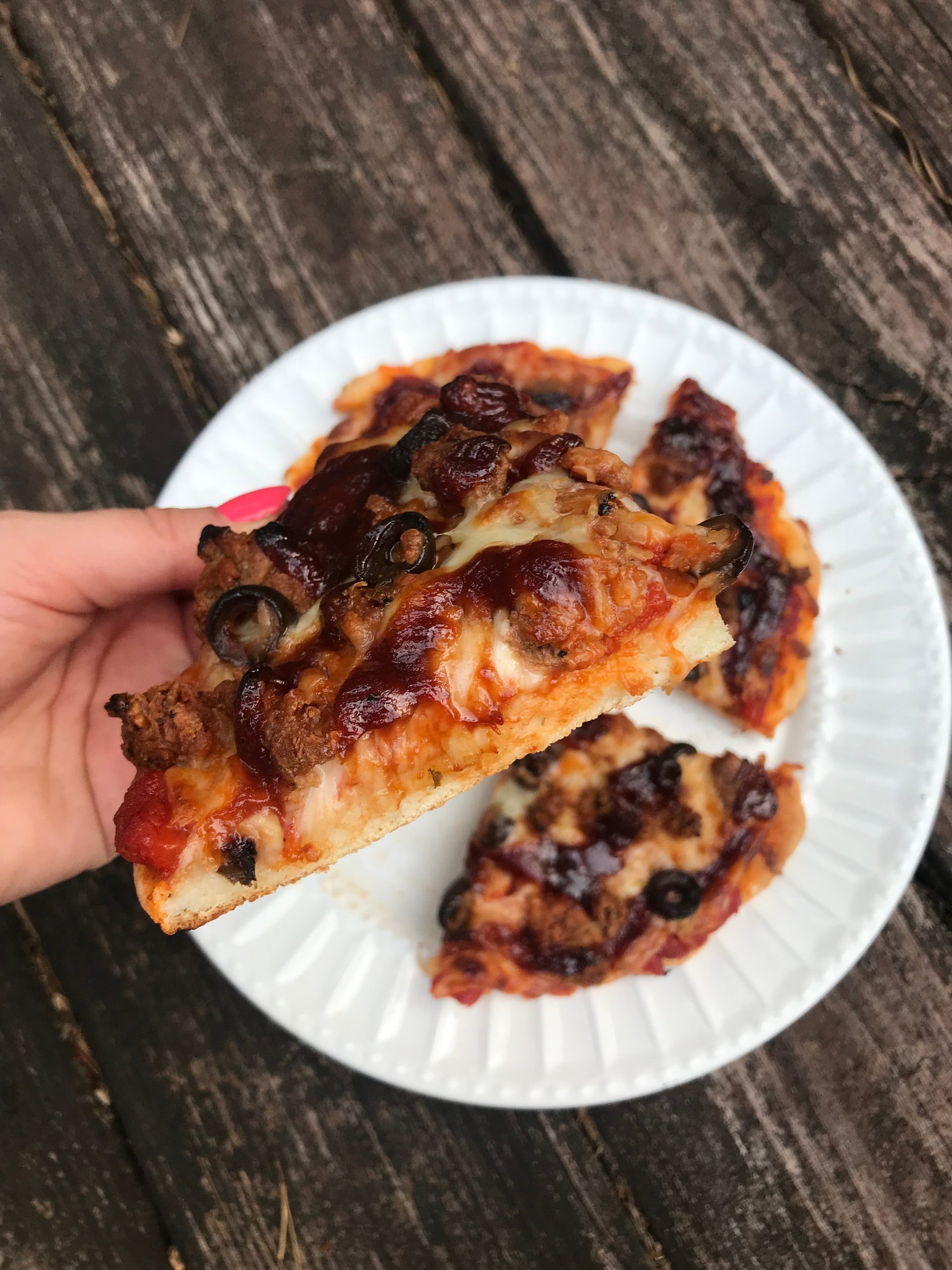 a hand holding up a piece of pizza over a plate of the rest of the pieces