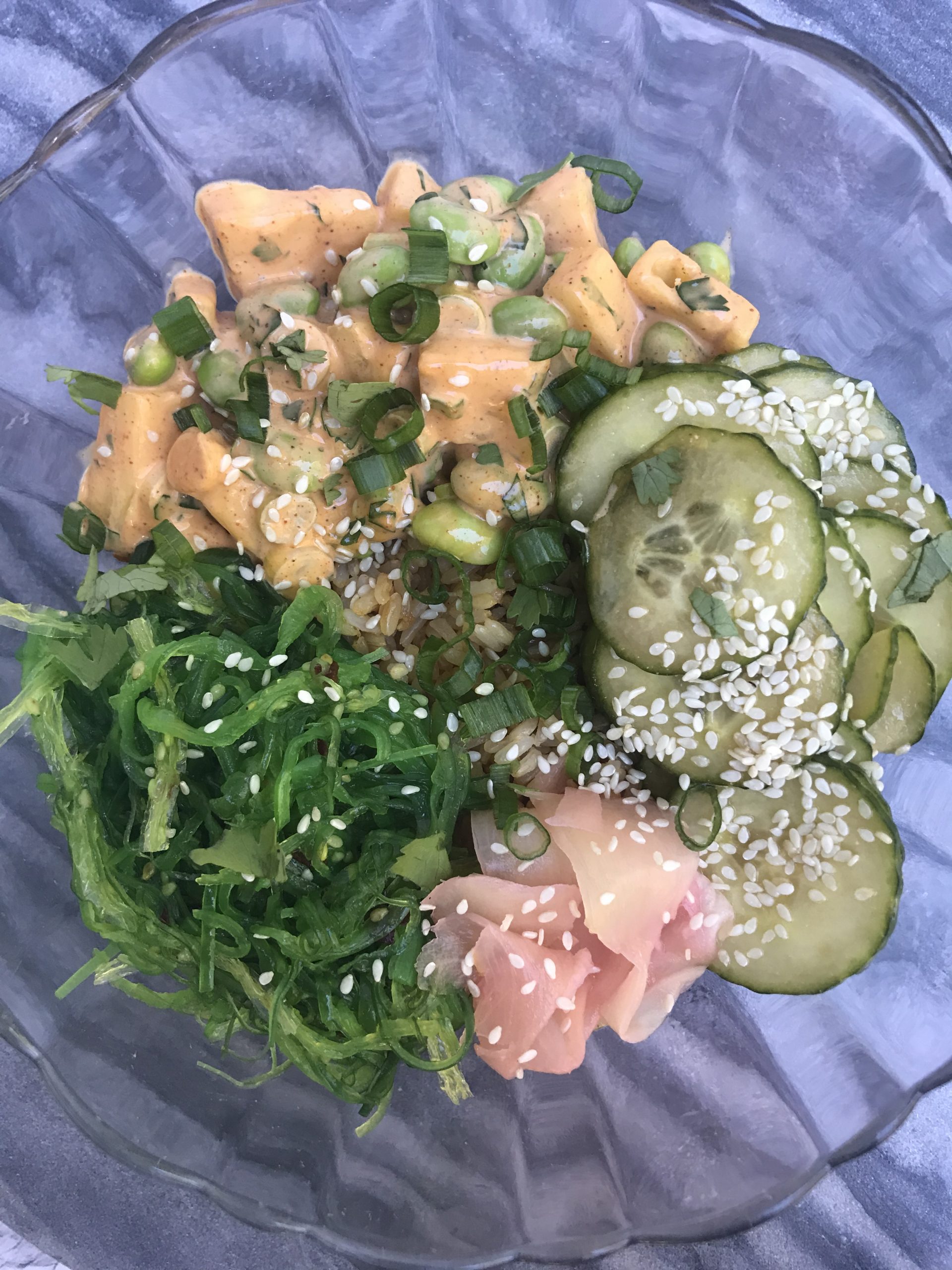 a poke bowl with rice, cucumber salad, and seaweed salad