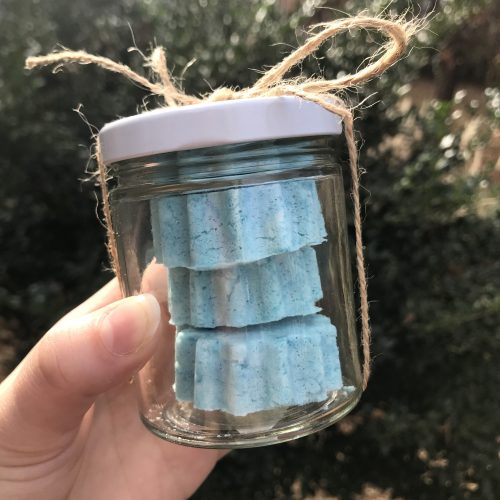 A hand holding up a glass jar filled with blue bath bombs.