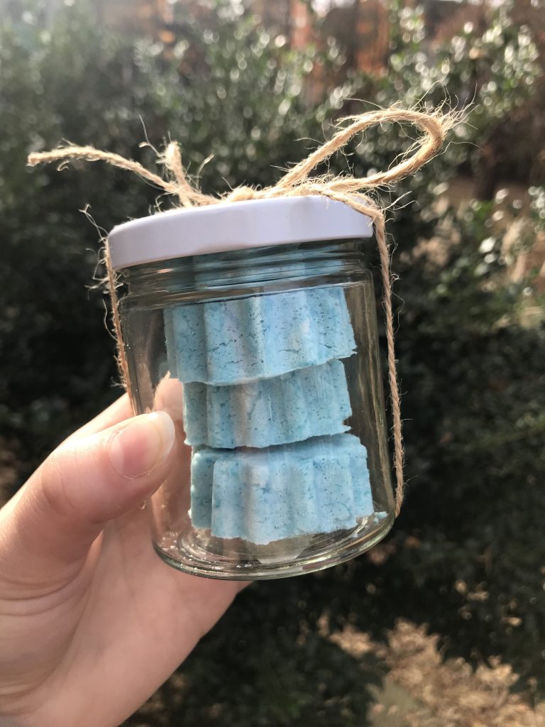 A hand holding up a glass jar filled with blue bath bombs.