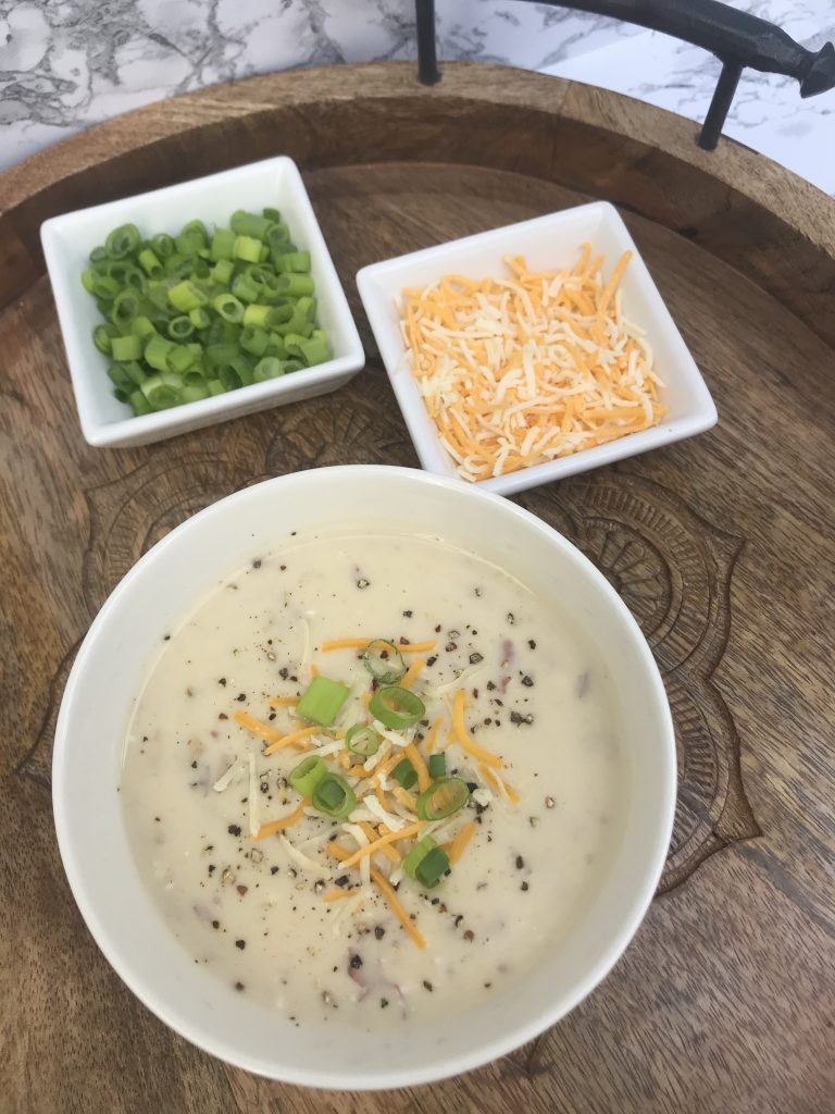 a bowl of potato soup with cheese and green onions on the side