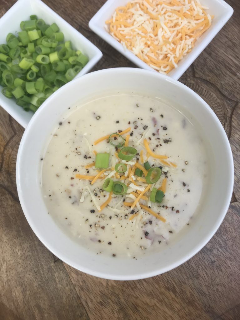 a bowl of potato soup with sides of cheese and green onions