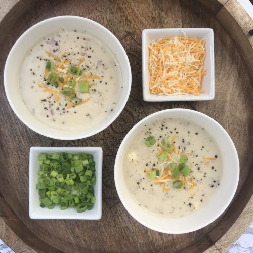 bowls of potato soup with sides of shredded cheese and diced green onions