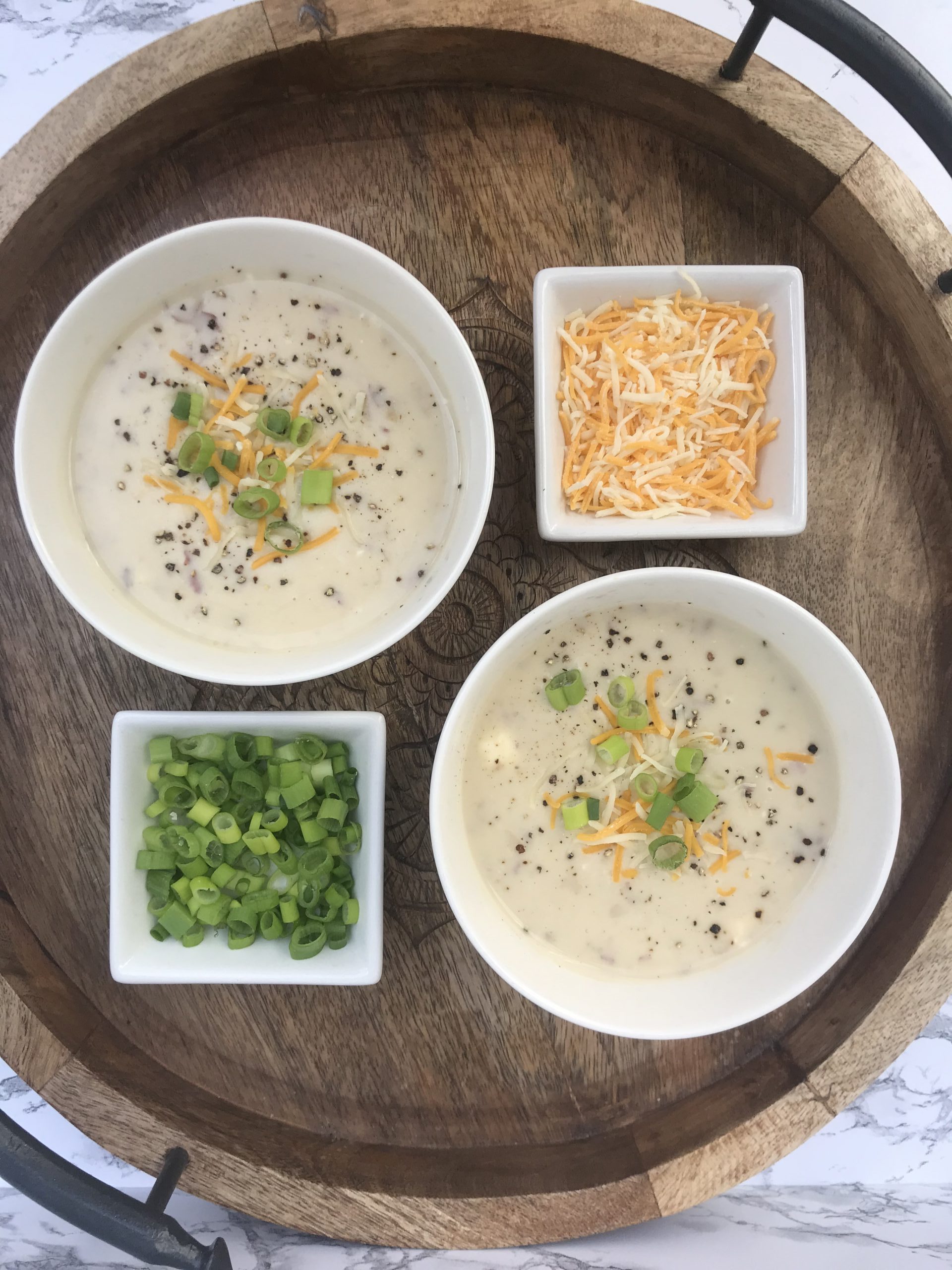 bowls of potato soup with sides of shredded cheese and diced green onions