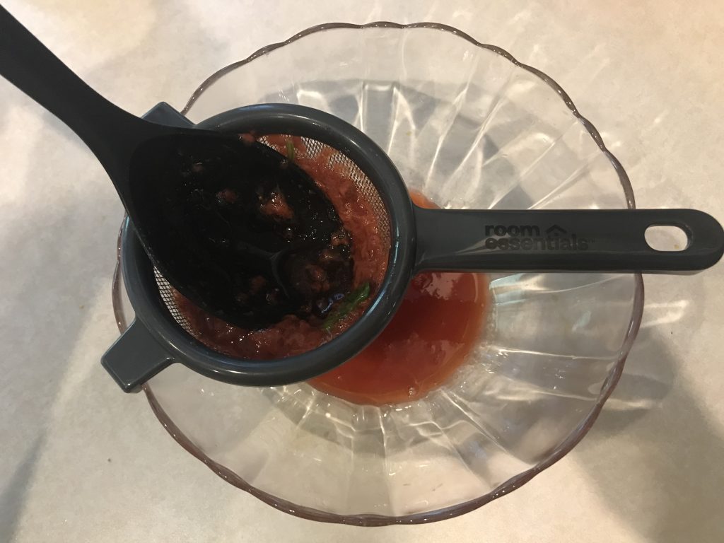 a spoon pressing the mixture through a mesh strainer into a bowl