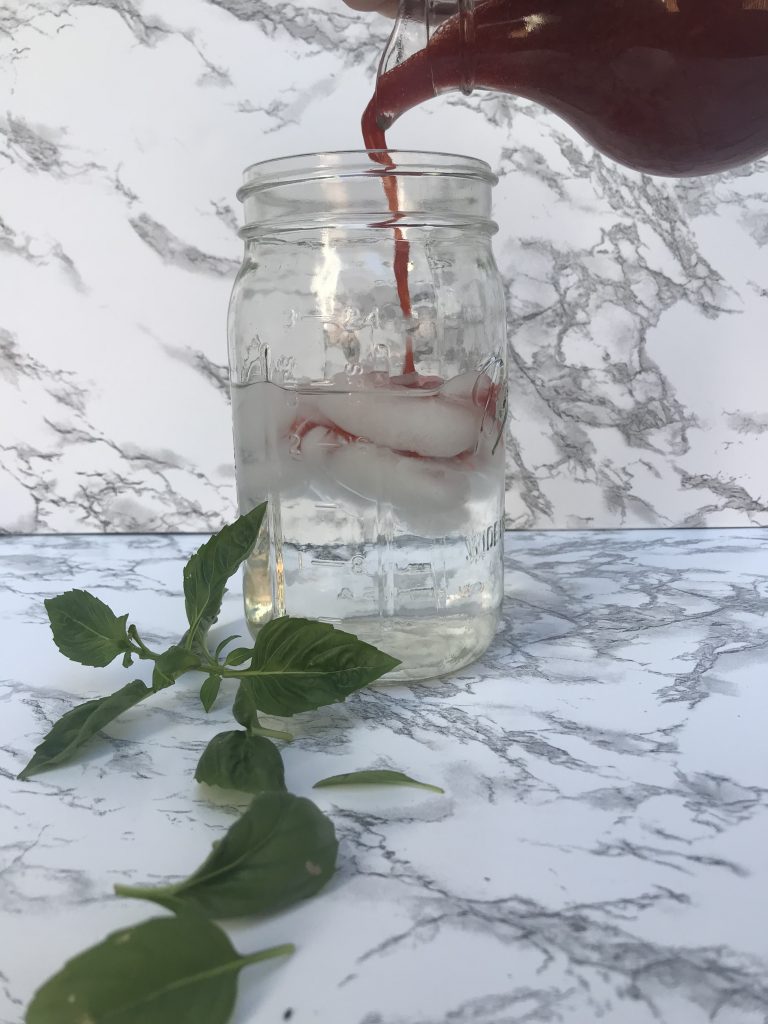 a bottle of syrup pouring into a glass of sparkling water