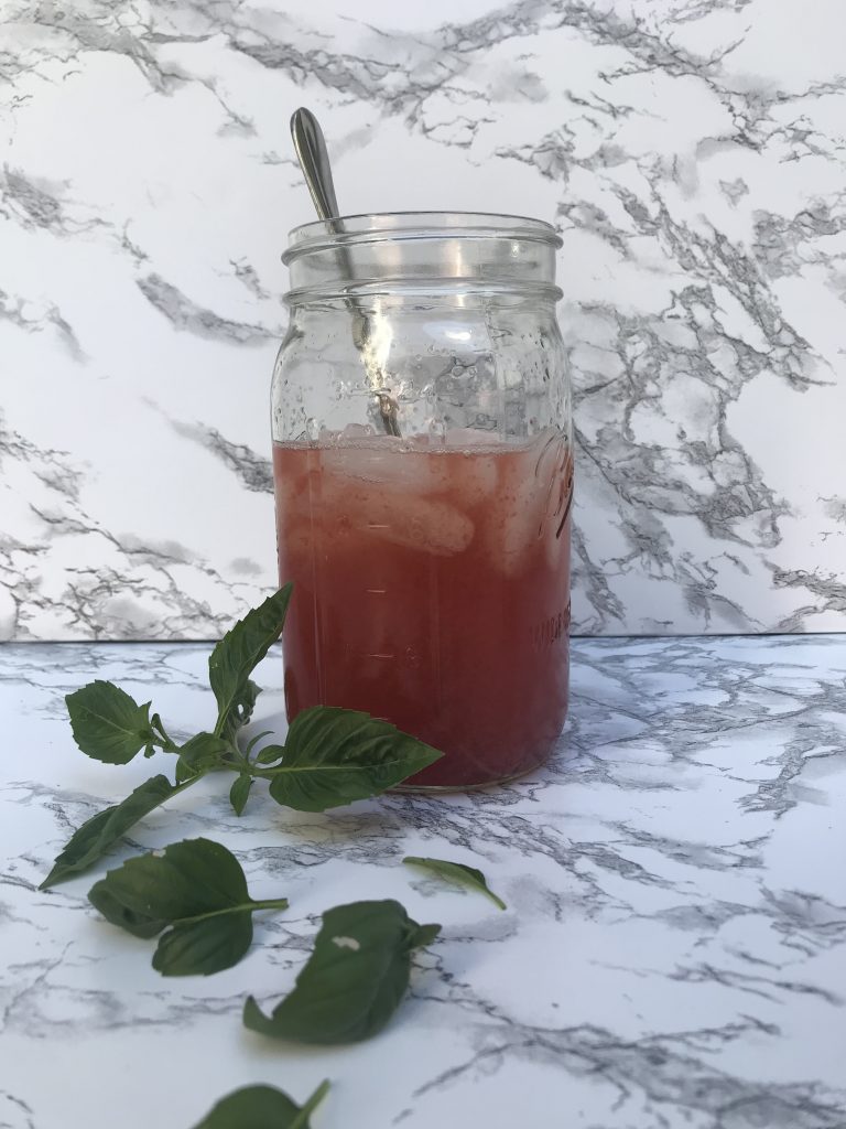 a jar of red sparkling water with a spoon and basil leaves