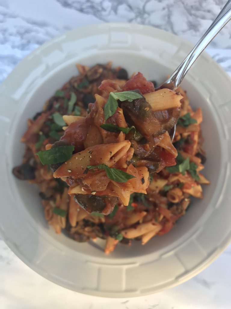 a serving bowl of pasta puttanesca with a spoon taking a scoop