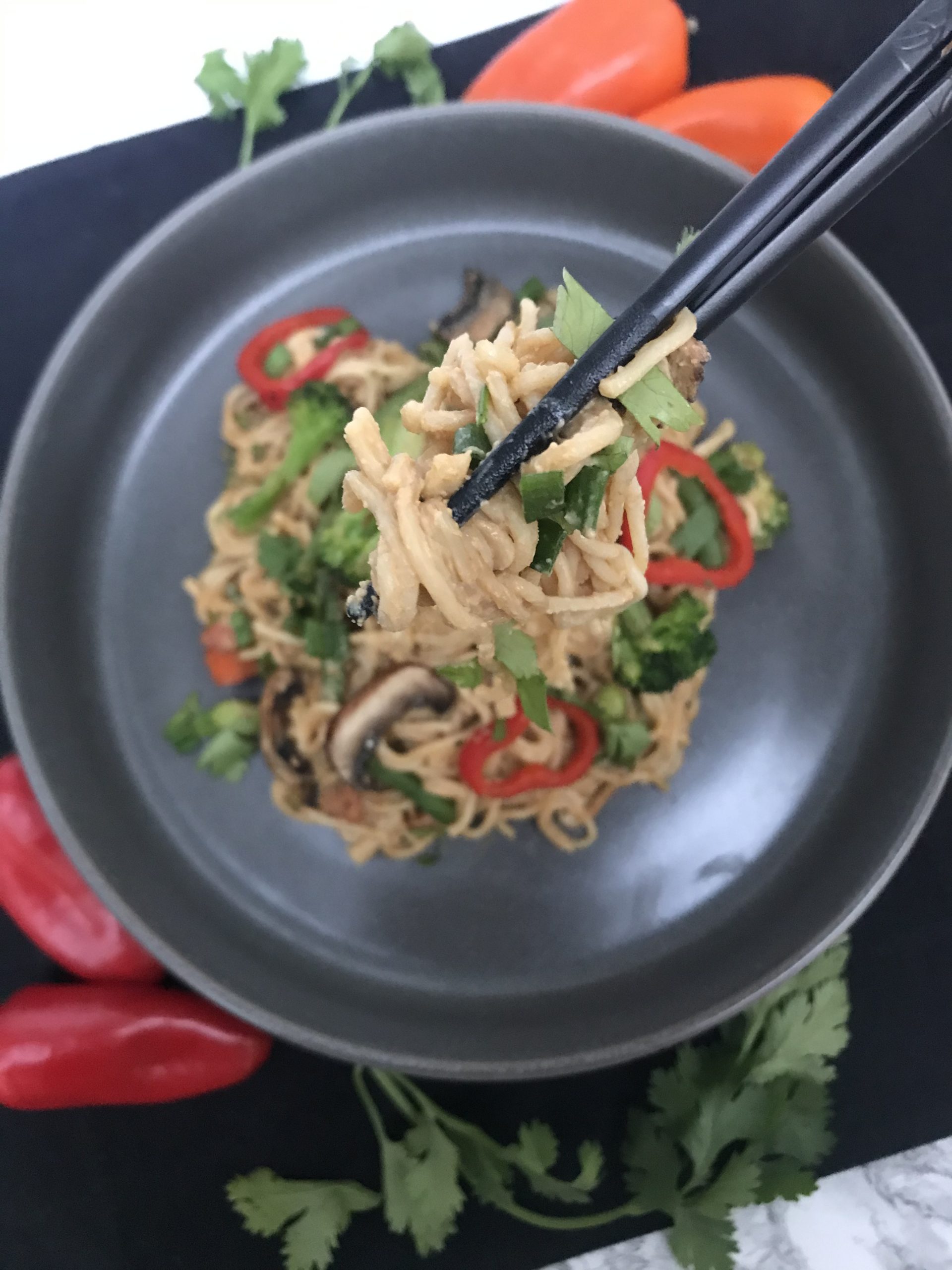 A plate of the cashew noodles anf veggies with chopsticks picking some noodles up