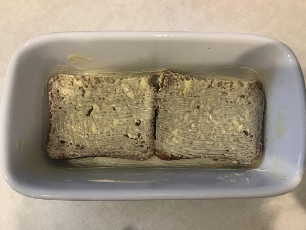 a loaf pan with buttered bread in the bottom