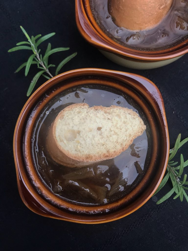 a crock of French onion soup with a slice of baguette in it