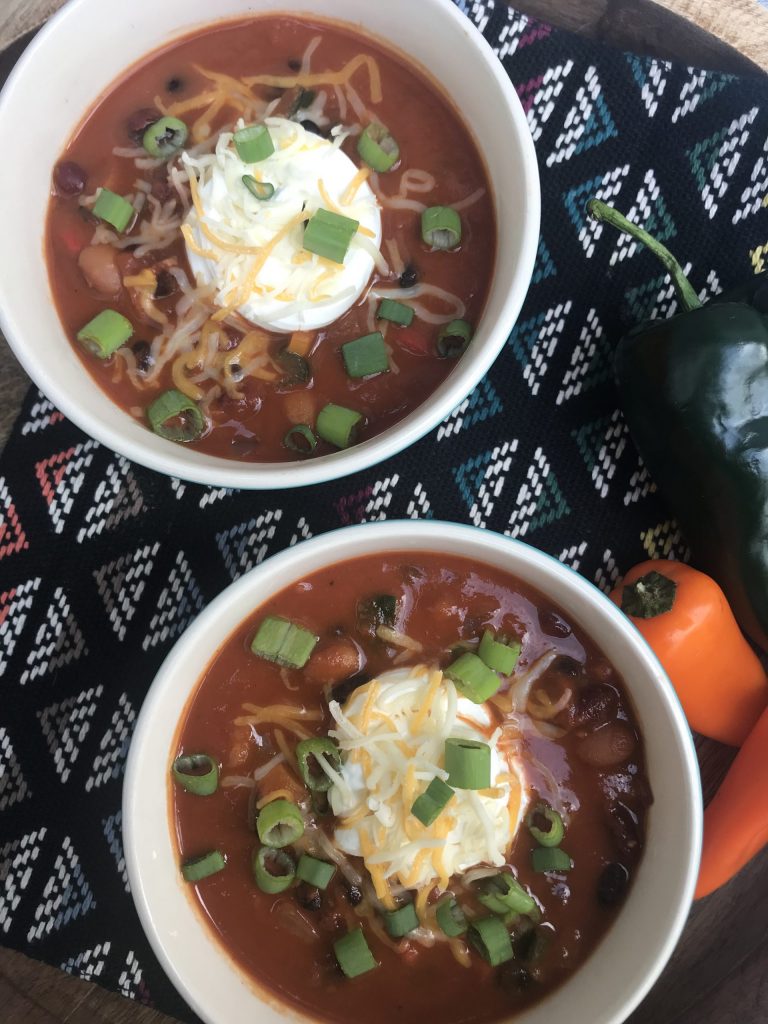 2 bowls of chili with a dollop of sour cream, shredded cheese, and green onions