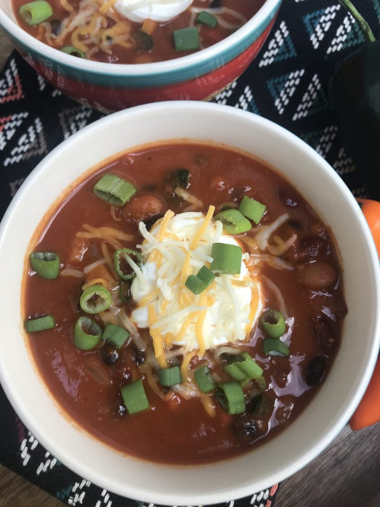 a bowl of chili with a dollop of soup cream, cheese, and green onions