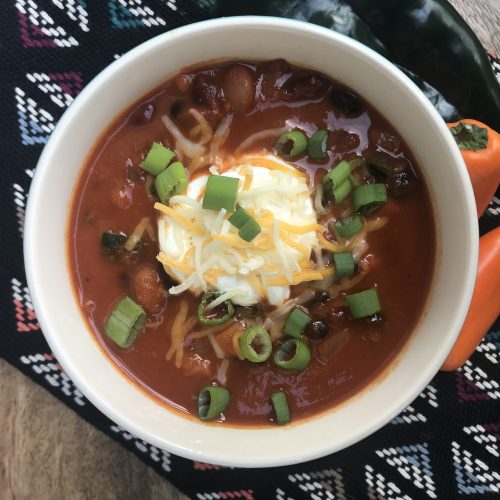 a bowl of chili with a dollop of sour cream, shredded cheese, and green onions