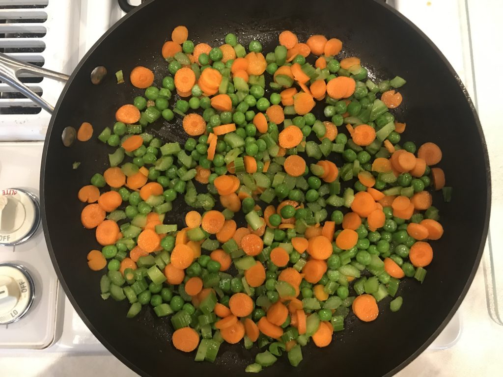 a pan with sliced carrots, celery, and peas