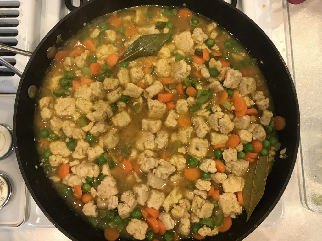 A pan with veggies, quorn chunks, broth, and bay leaves