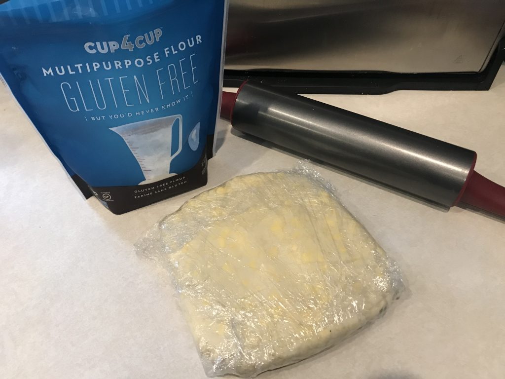 the puff pastry wrapped in cling wrap with the rolling pin and four in the background