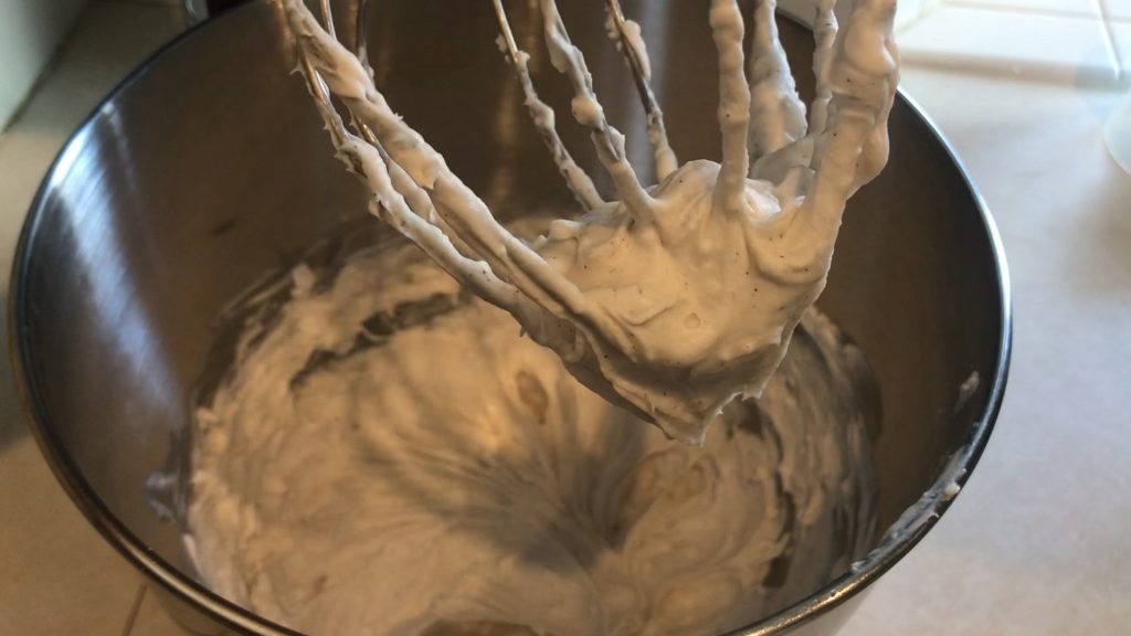 a bowl of whipped coconut cream with a soft peak on the whisk