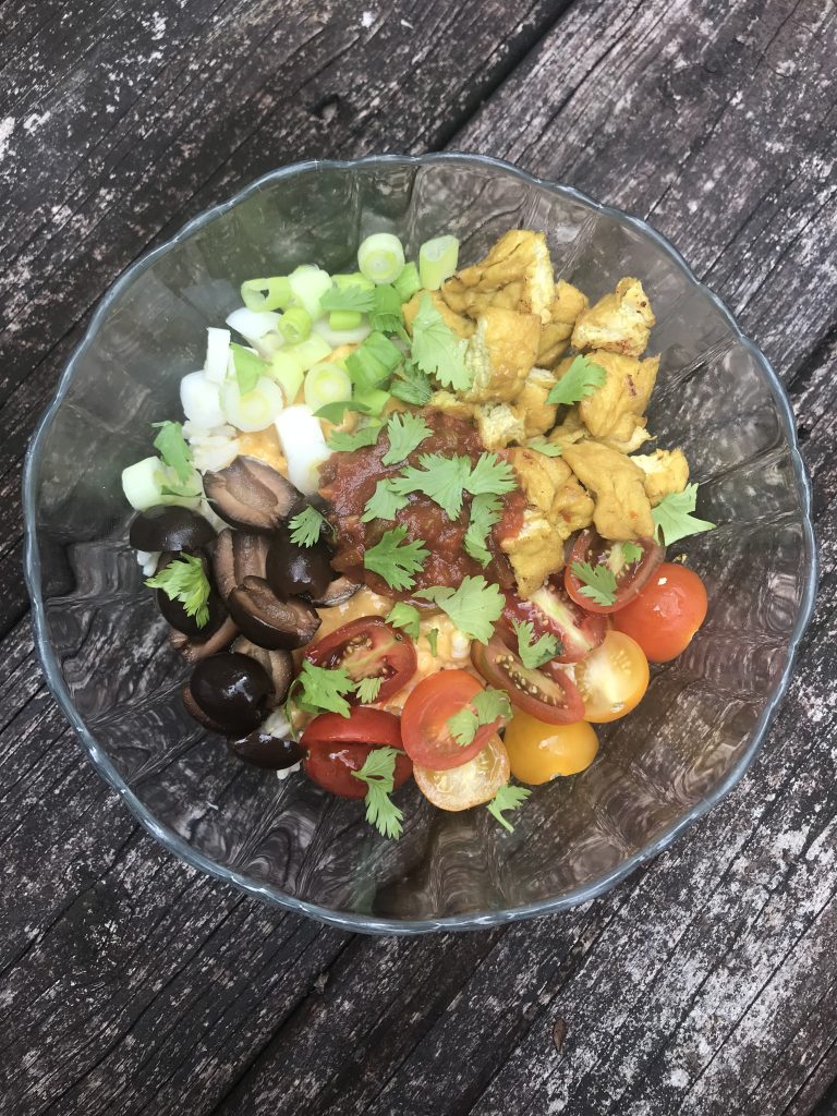 a rice bowl with green onions, olives, tomatoes, tofu nugget, and cilantro