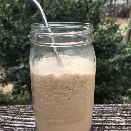 A jar of blended protein coffee with a metal straw in it