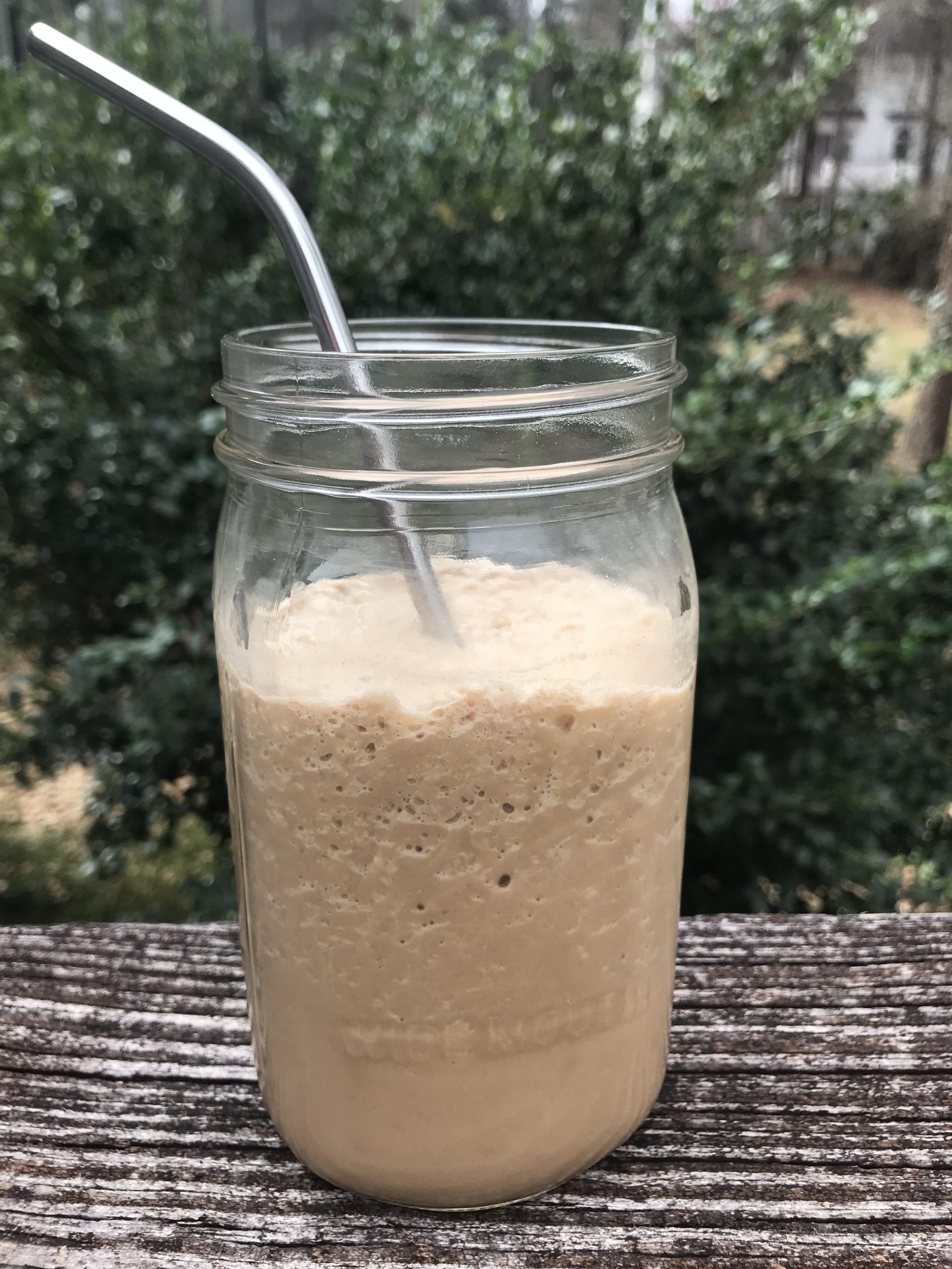 A jar of blended protein coffee with a metal straw in it