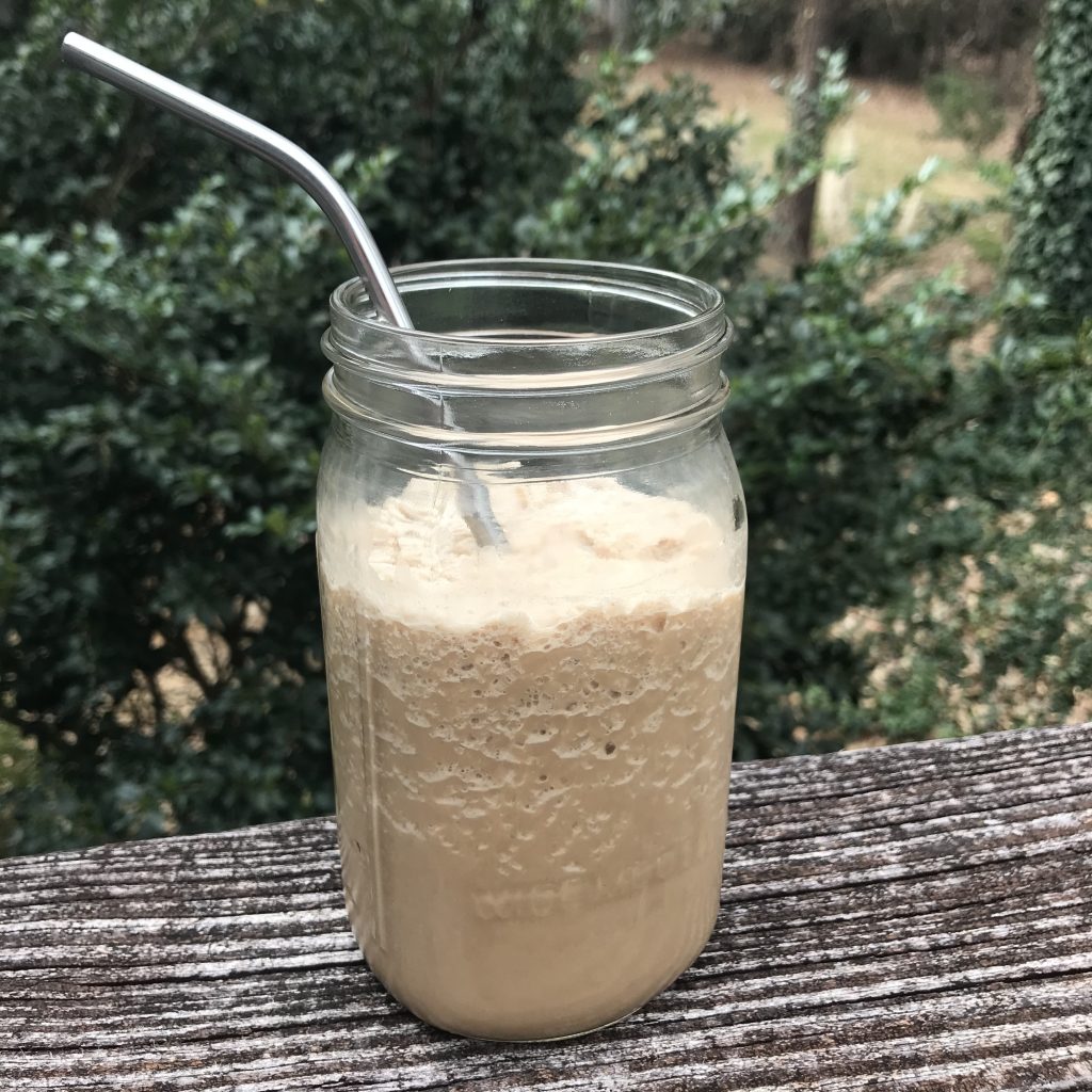 A jar of blended protein coffee with a metal straw in it