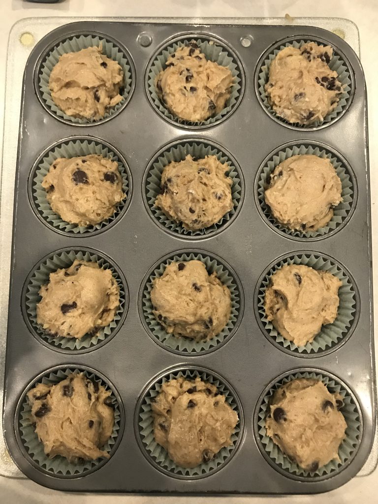 a tray of uncooked muffins in paper liners