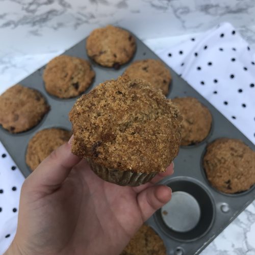 a hand holding up a muffin with the tray in the background