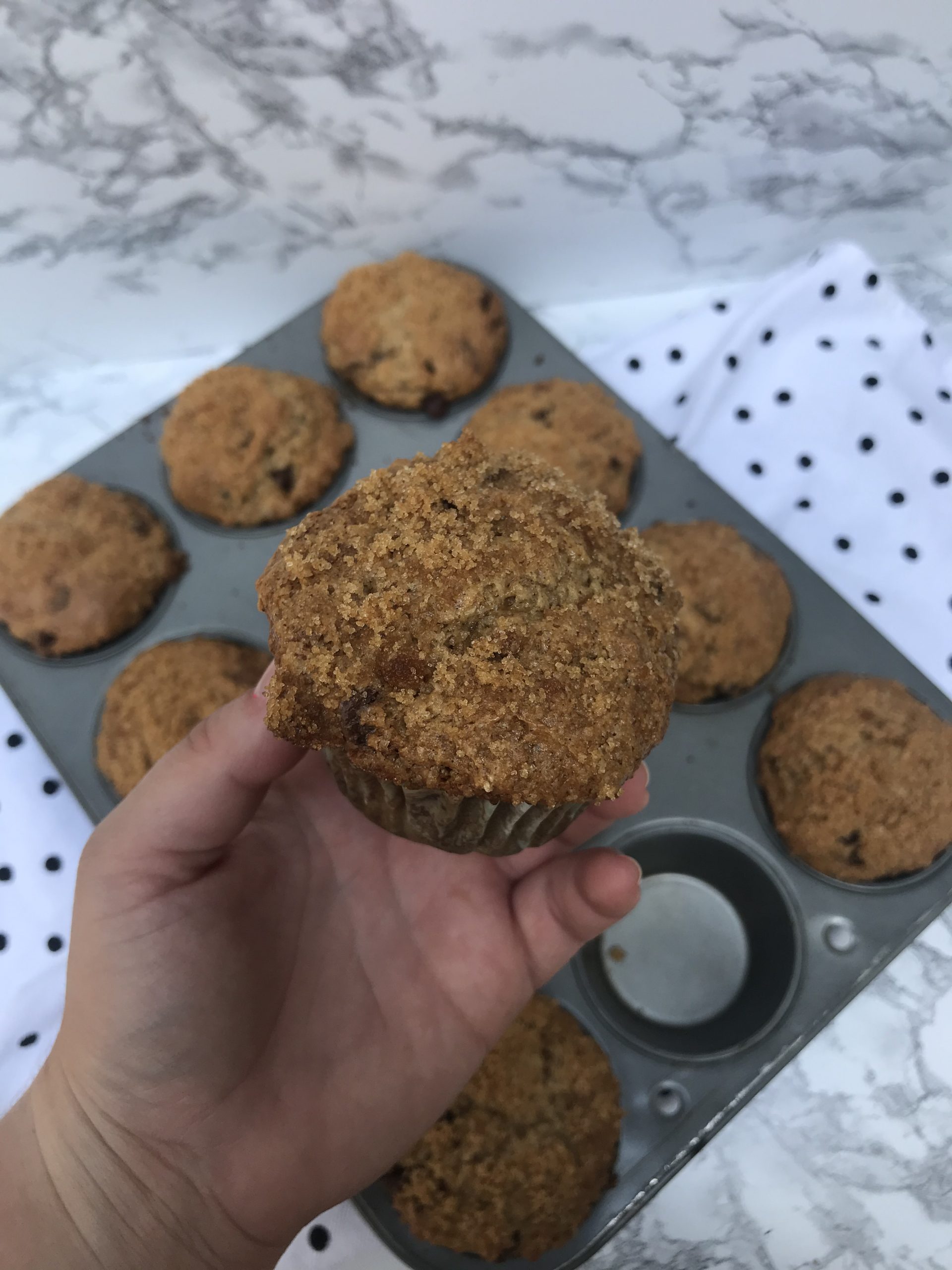 a hand holding up a muffin with the tray in the background