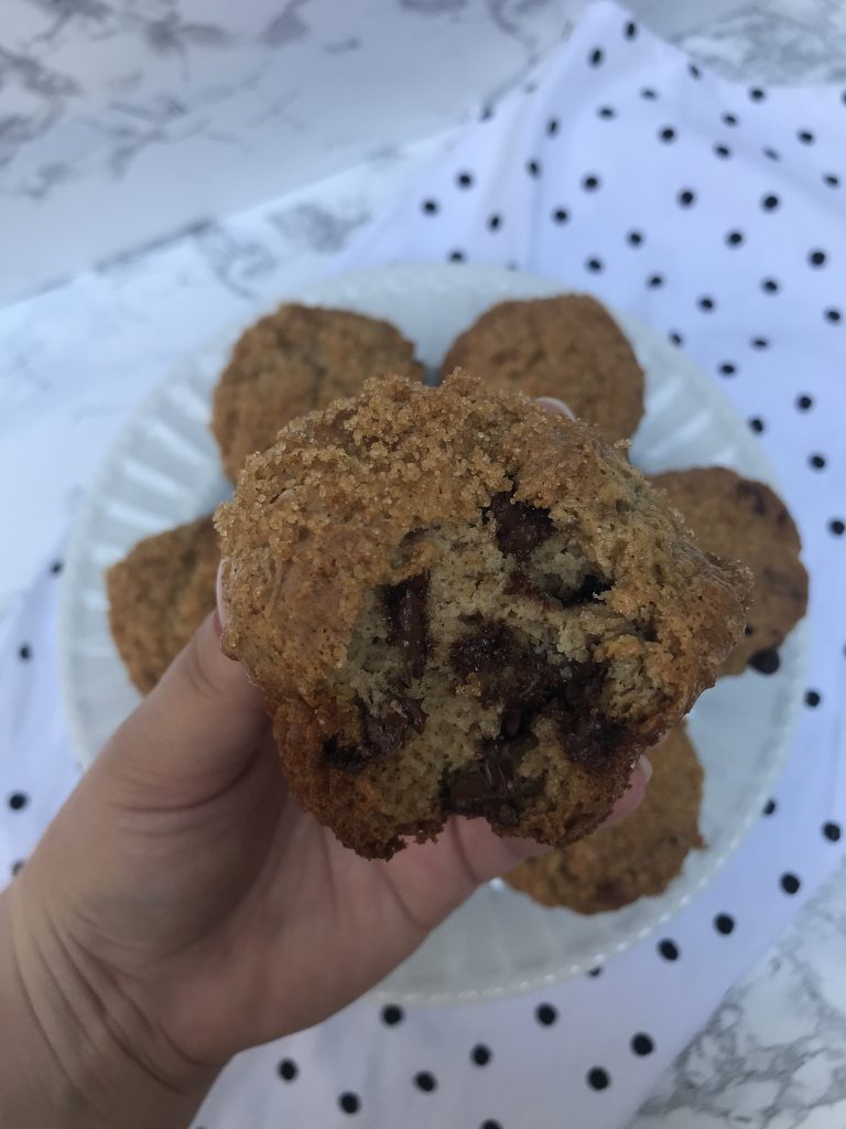 a hand holding a muffin up with a bite taken out showing the chocolate chips inside