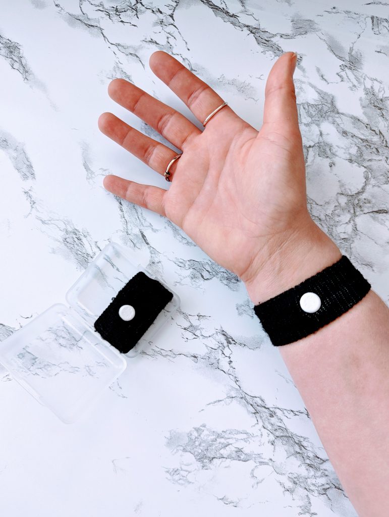 a white hand with the black sea band around the wrist. The white acupressure point is centered on the inside of the wrist.