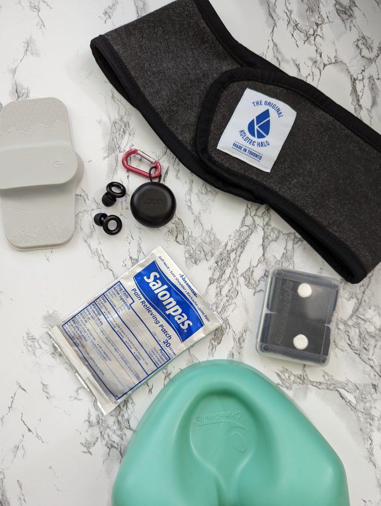 a flat lay of migraine tools including salonpas, seabands, ear plugs, nerivio, and a icepack headband