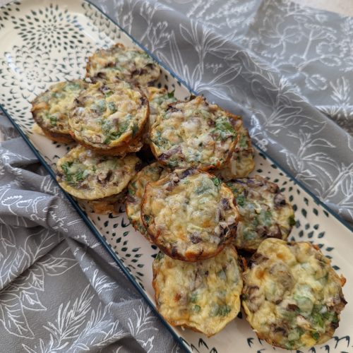 A tray on top of a grey tea towel with the spinach and mushrooms breakfast muffins stacked up