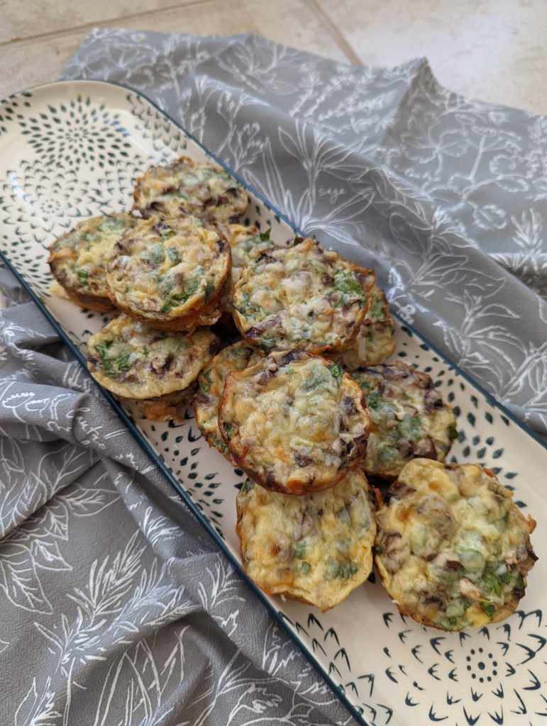 A tray on top of a grey tea towel with the spinach and mushrooms breakfast muffins stacked up